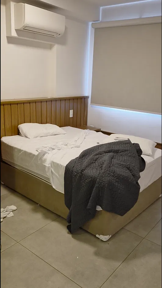 Quarto do apartamento na manhã seguinte, com cama desfeita e roupas no chão